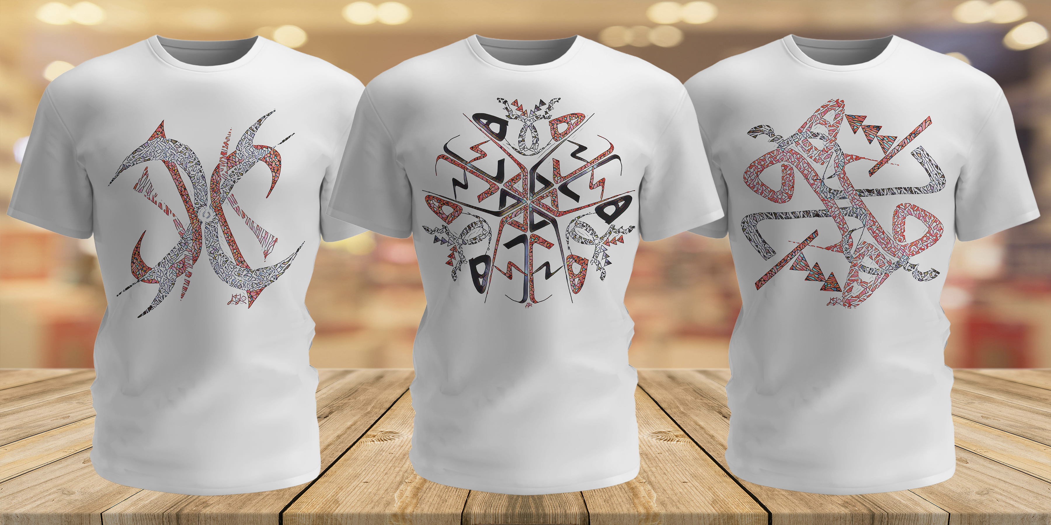 Three white t-shirts with tribal designs on a wooden surface.